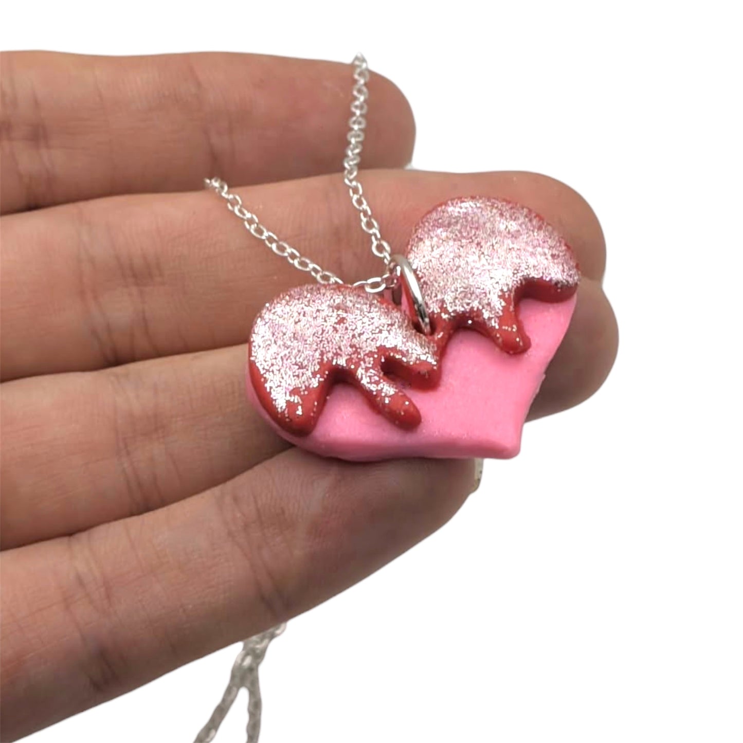 Pink heart-shaped necklace with red and silver details held in a hand against a white background