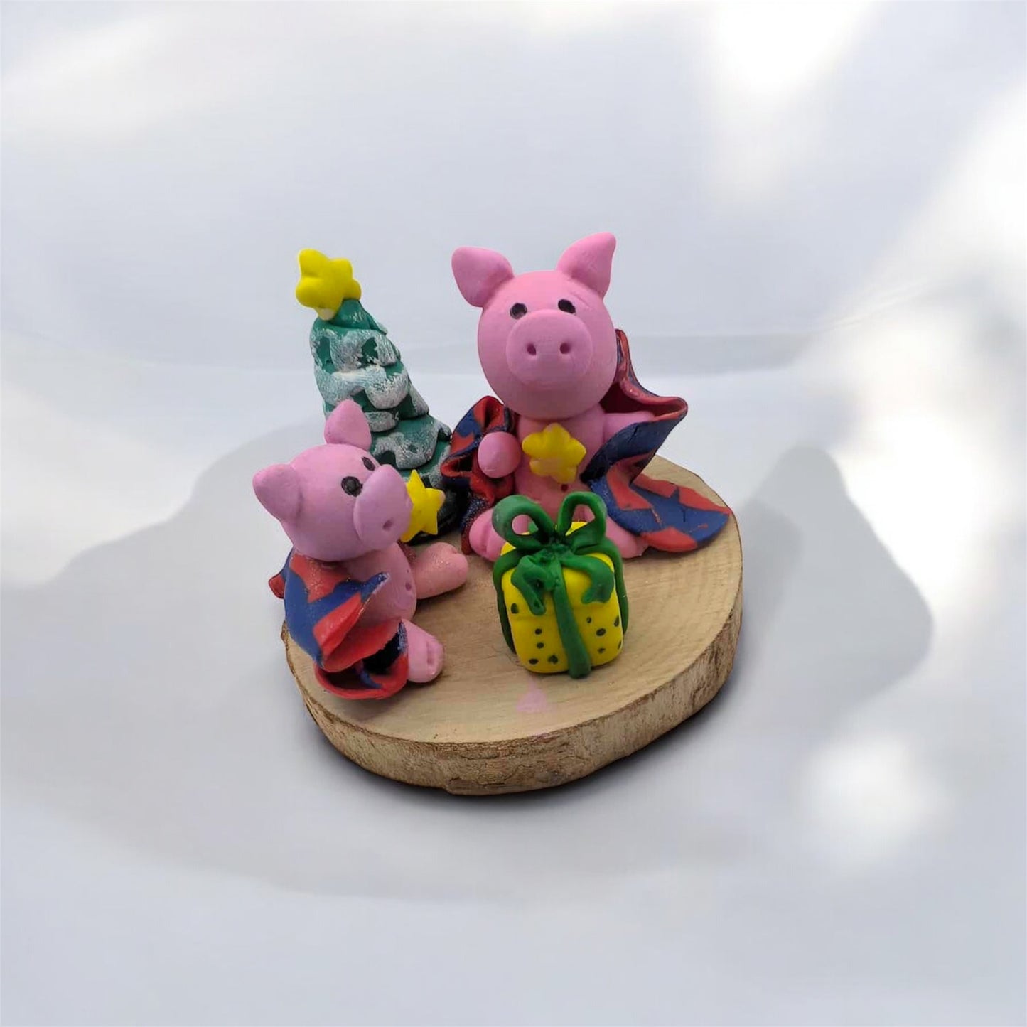 Two pink pig figurines with blankets Christmas-themed accessories on a wooden base