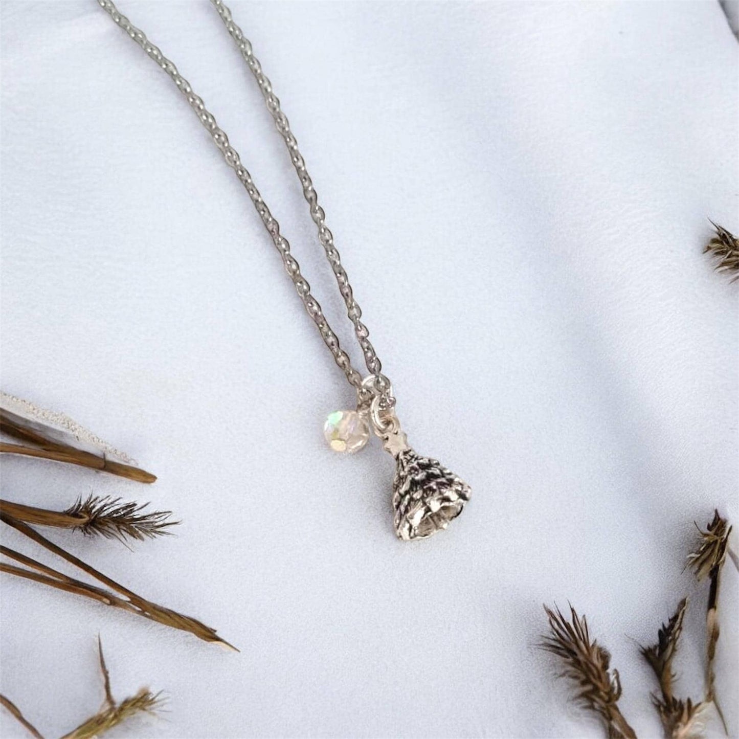 Necklace with a pine cone pendant on a white background with dried plants.