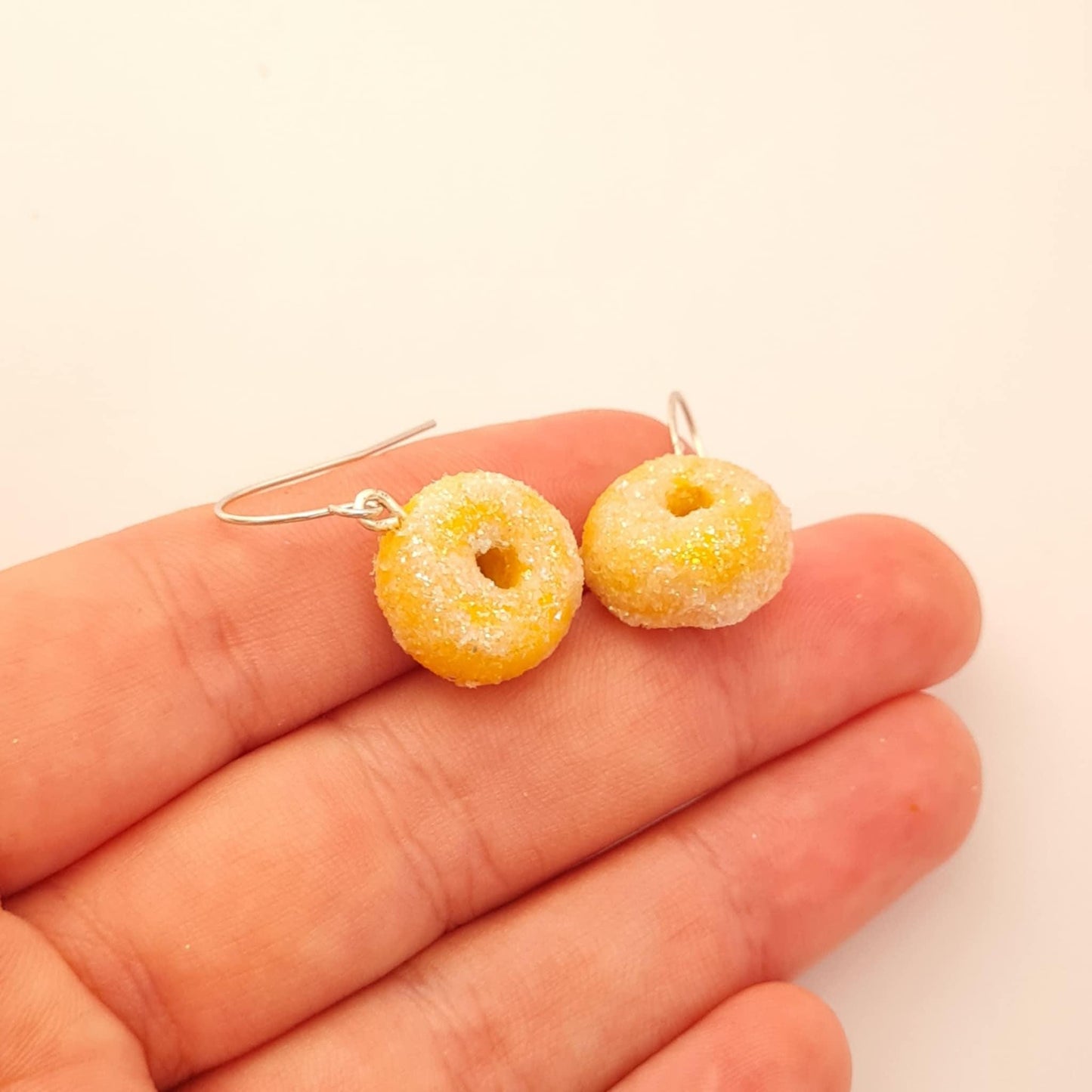 Donut-shaped earrings held between fingers on a light background