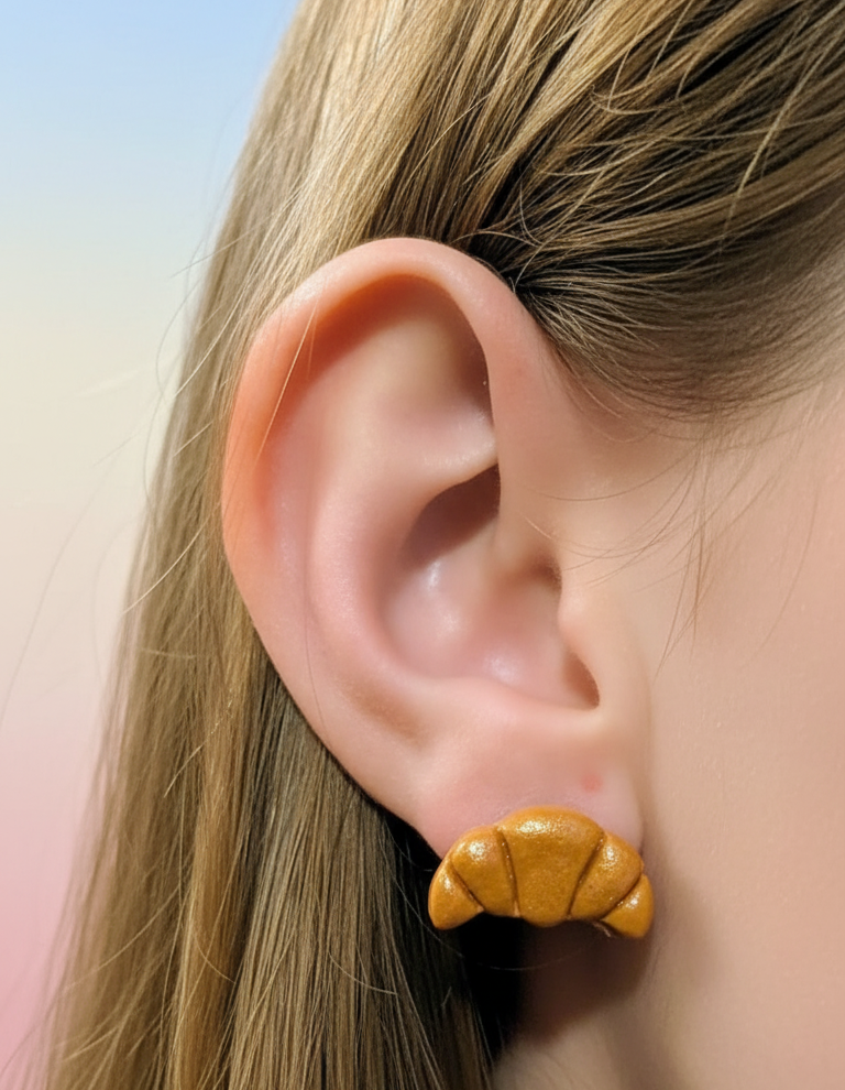 Croissant stud earring worn in earlobe on pastel background