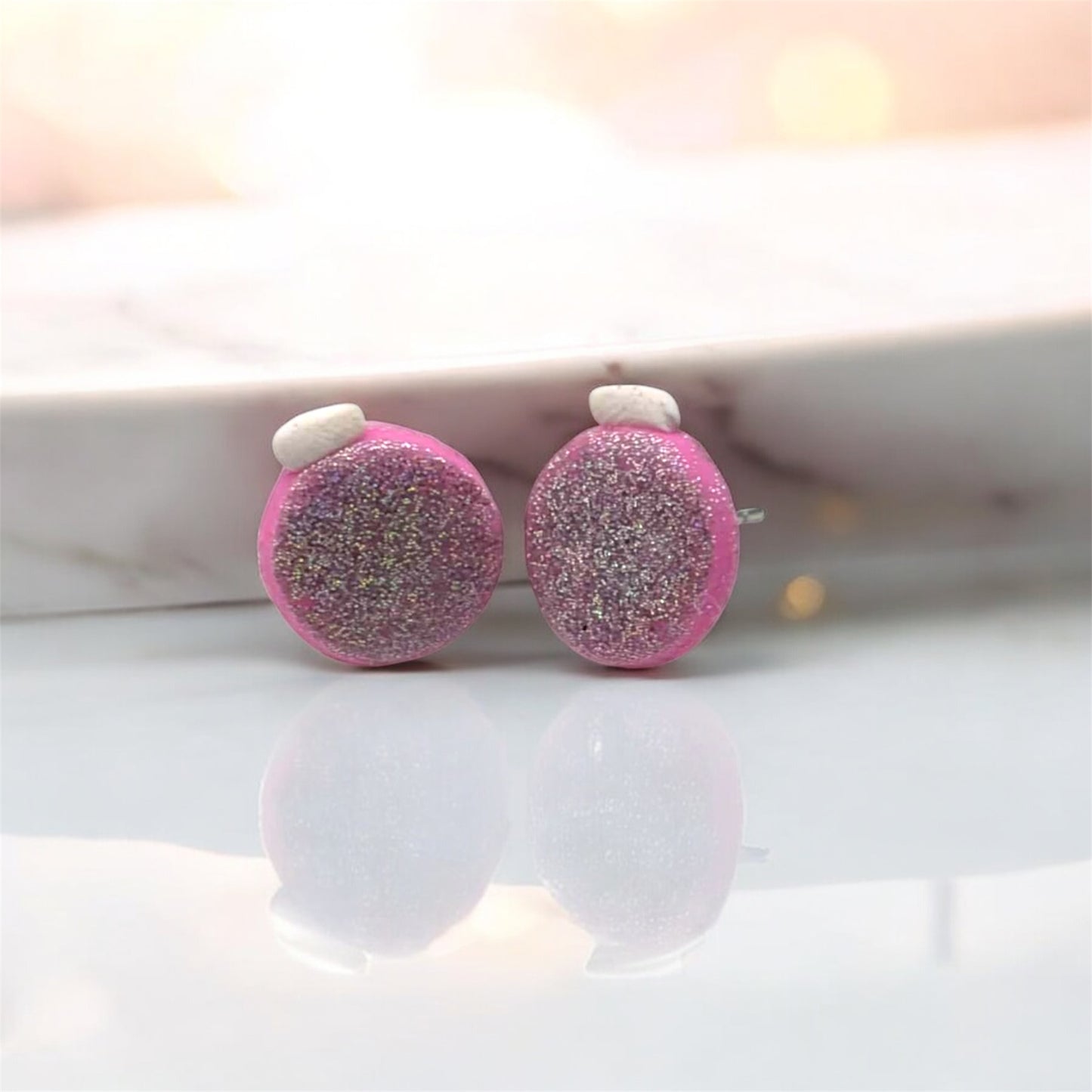 Pink glittery earrings on a white surface with a blurred background