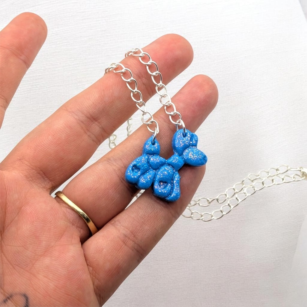Sparkling blue balloon dog necklace on a pale background