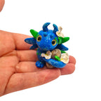 Small blue and green dragon figurine held in a hand against a white background