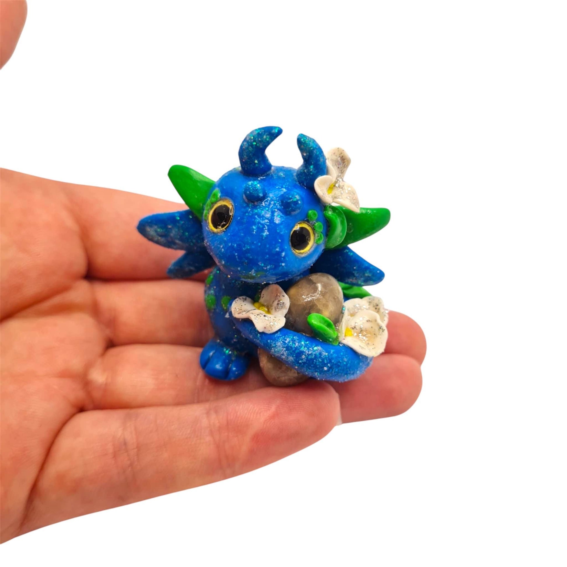 Small blue and green dragon figurine held in a hand against a white background