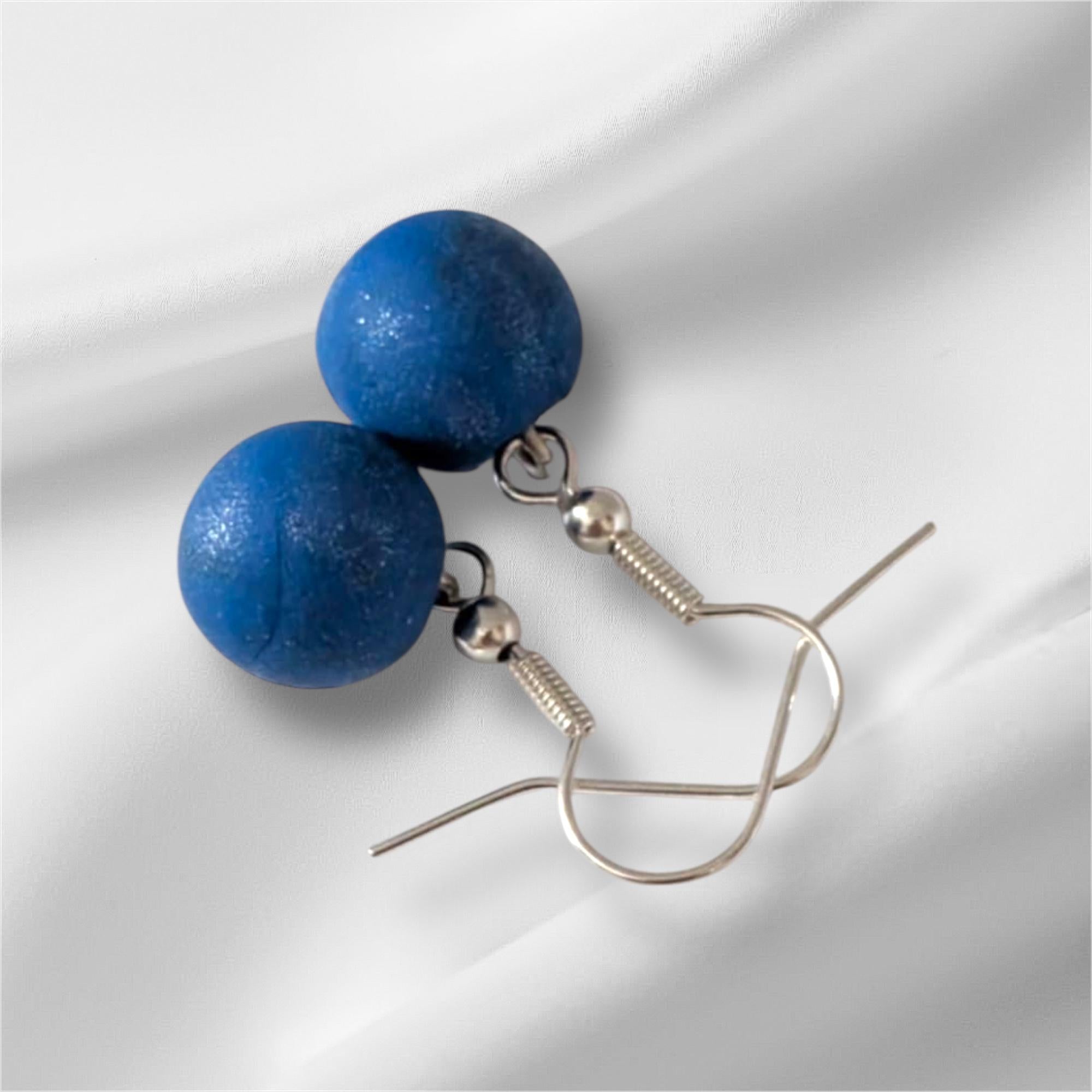 Blue berry earrings on a white fabric background