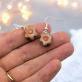 Flower-shaped earrings with a pink center held between fingers against a blurred light background