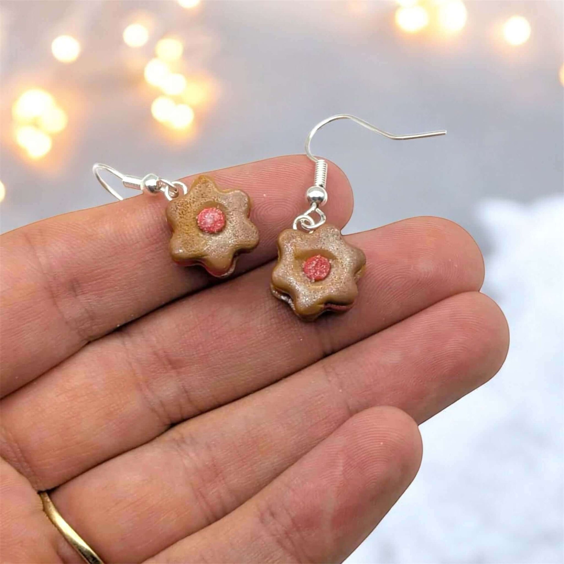 Flower-shaped earrings with a pink center held between fingers against a blurred light background