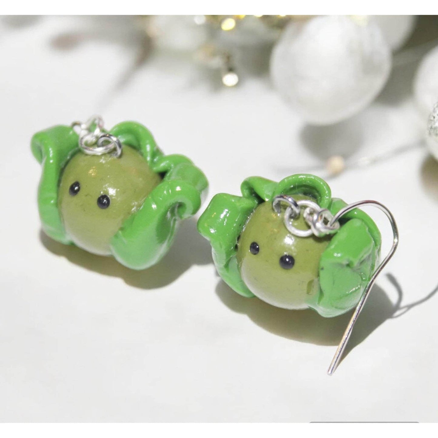 Green brussel sprout earrings on a white surface 
