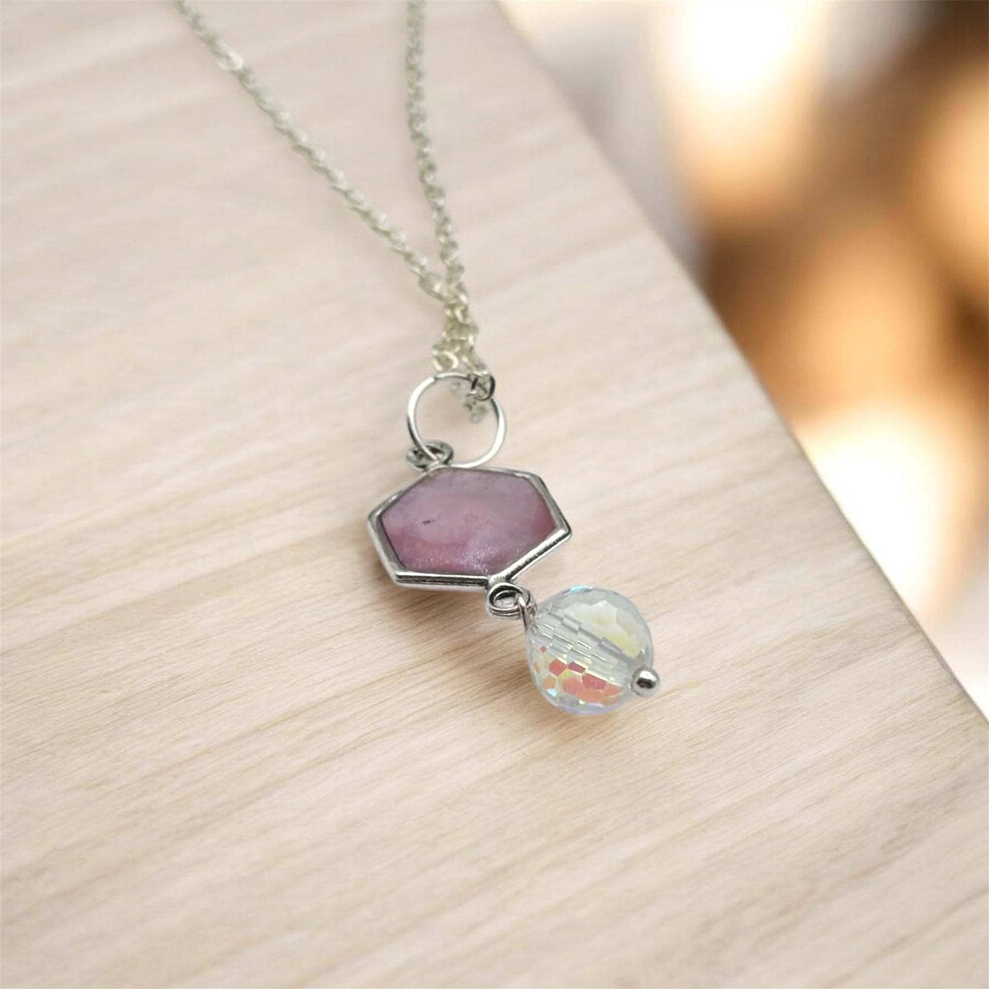 Necklace with a pink hexagonal pendant and a round clear crystal on a light wooden surface.