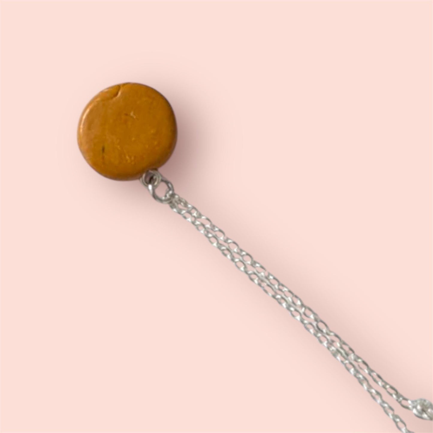 Back of cookie brown round pendant on a chain against a pink background