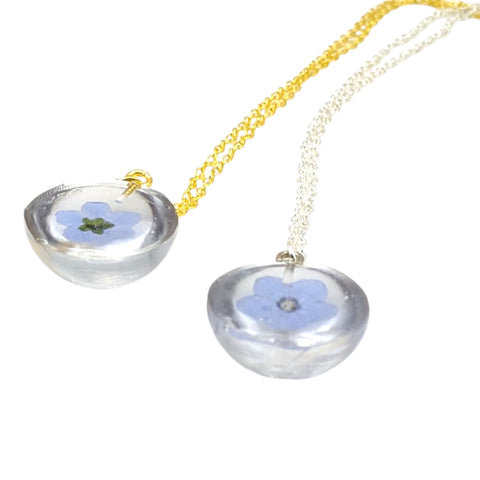 Back of Necklace with clear pendant holding a blue flower on a white background