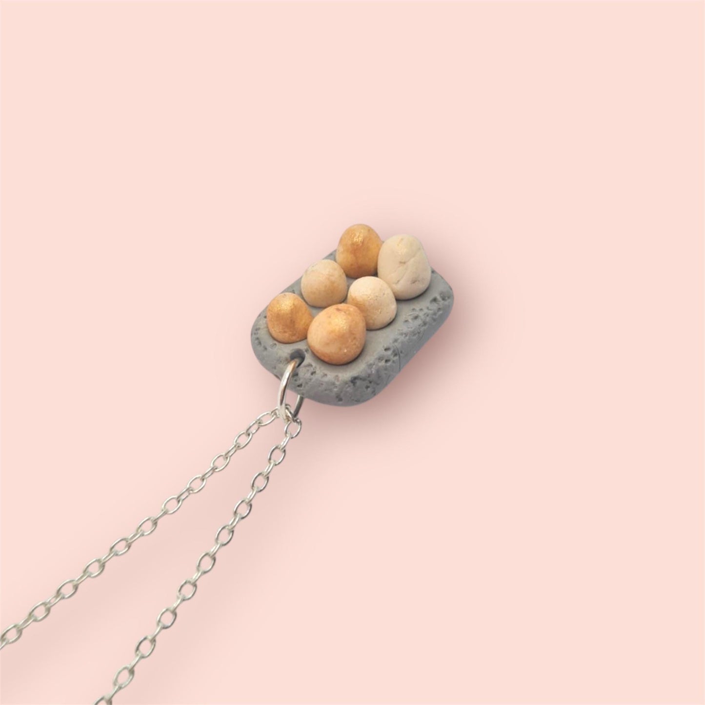 Miniature eggs in a carton on a silver chain against a light pink background 