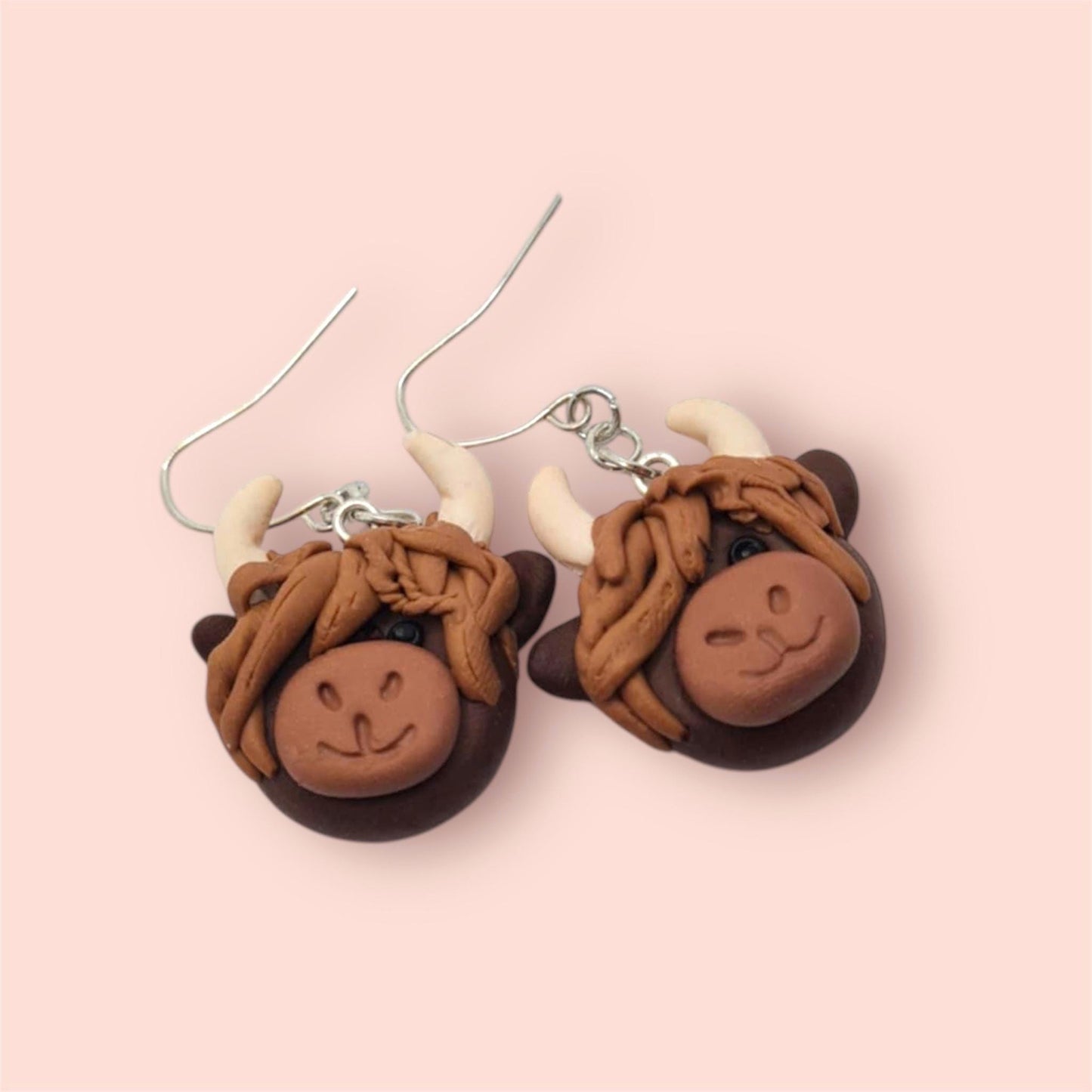 Highland cow-shaped earrings on a pink background