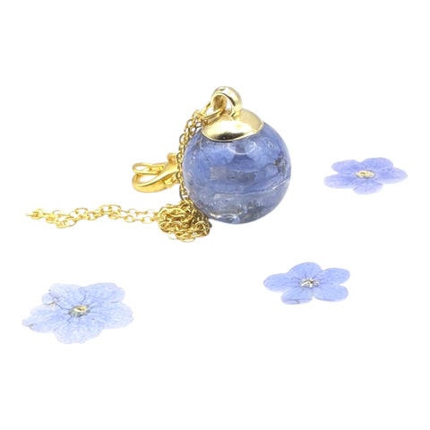 Blue flower glass pendant with gold chain on a white background with blue flowers.