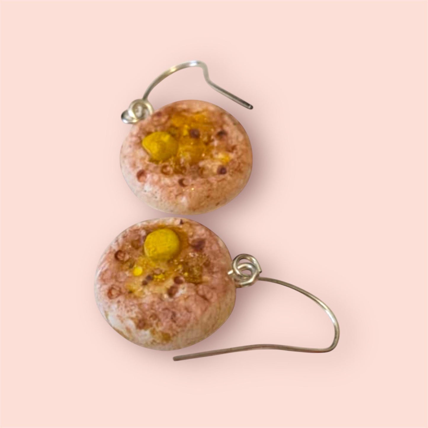 Round earrings with pink and yellow design on a light pink background