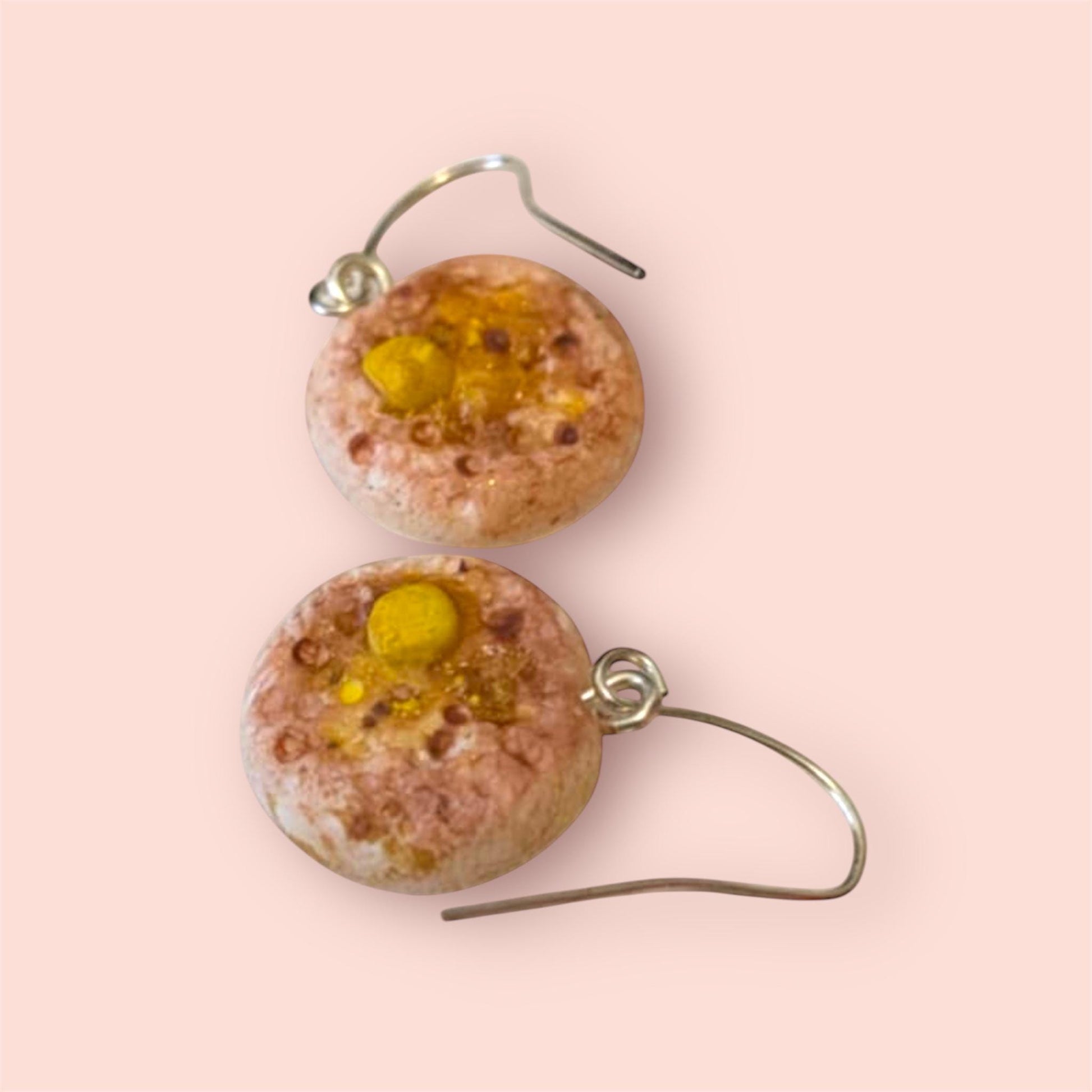 Round earrings with pink and yellow design on a light pink background