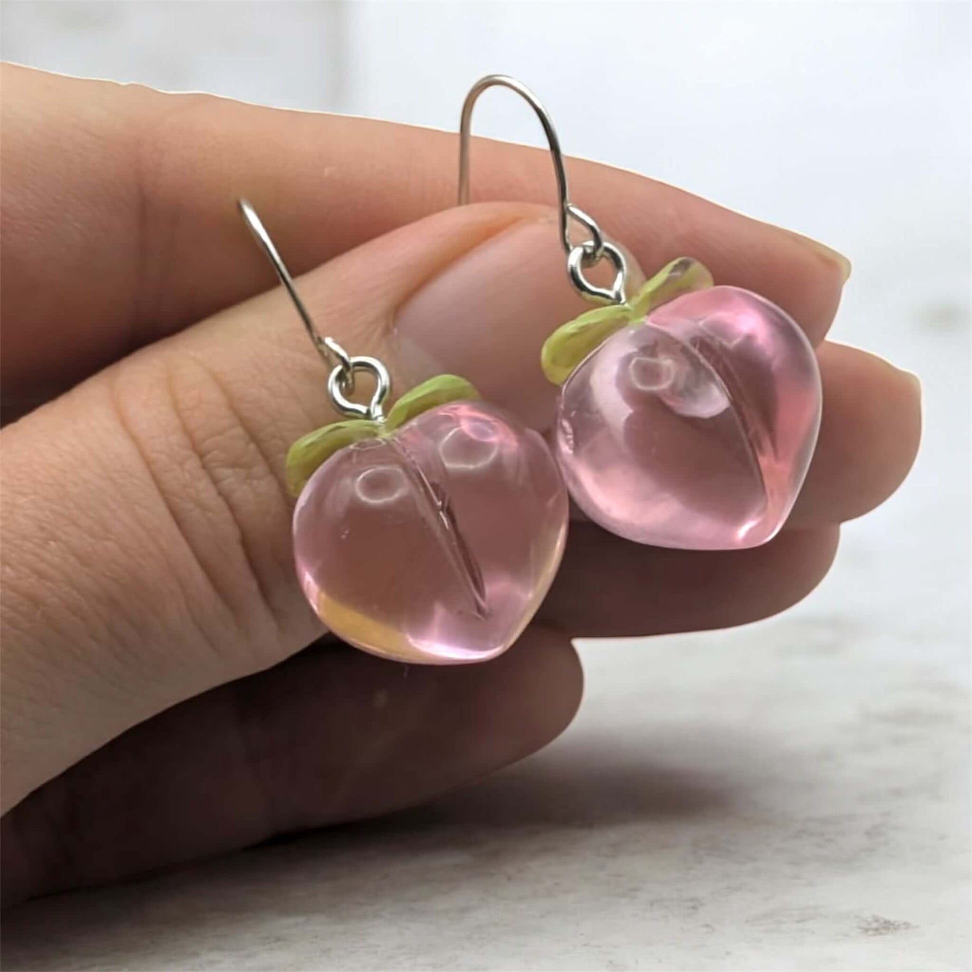 Peach earrings held in hand on a marble like background 