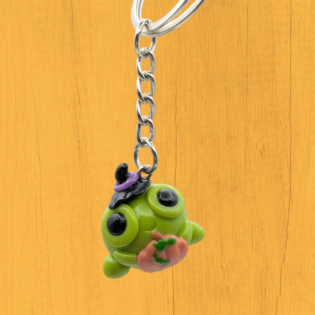 Kawaii Halloween frog keyring hanging, showing witch hat and pumpkin detail on orange background