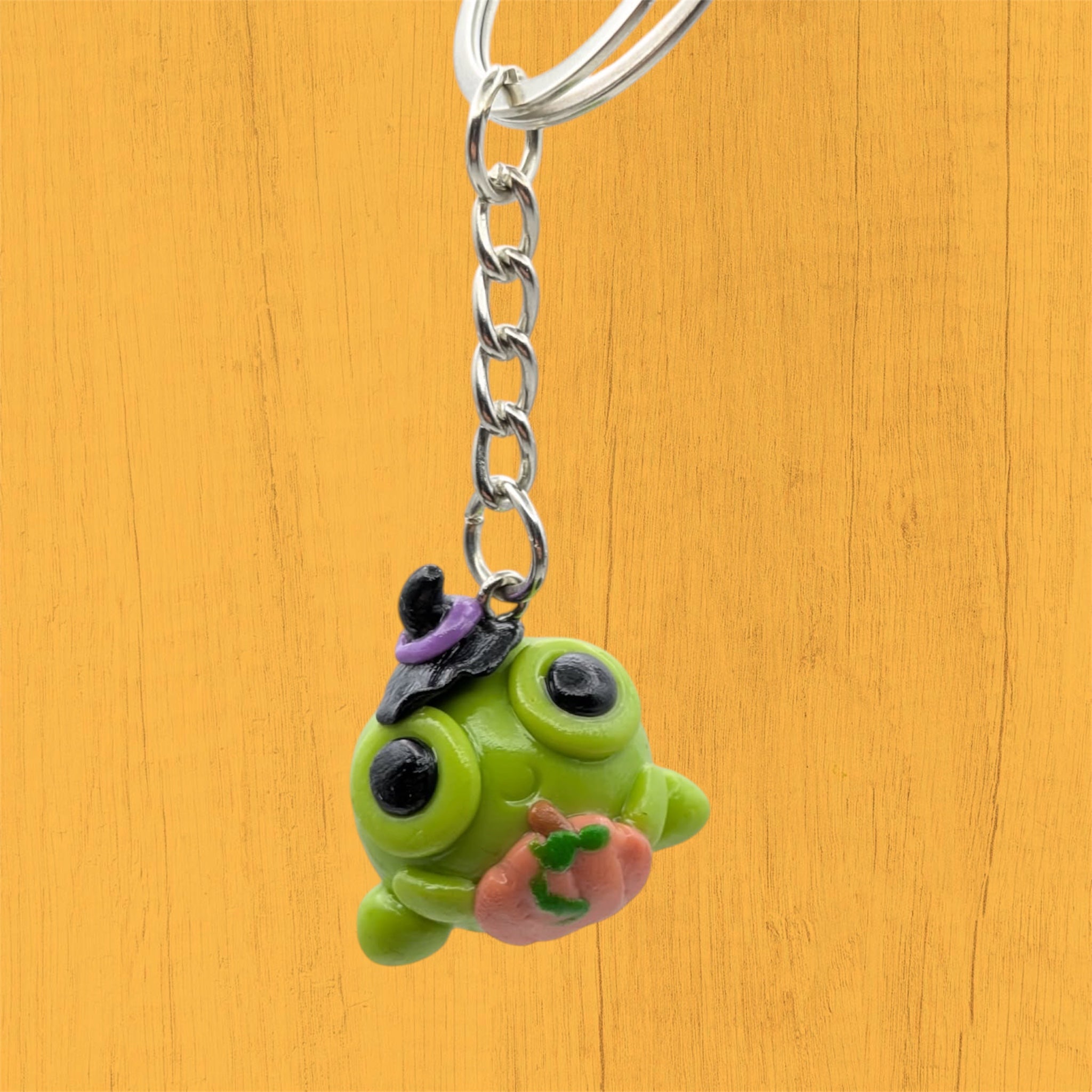 Kawaii Halloween frog keyring hanging, showing witch hat and pumpkin detail on orange background