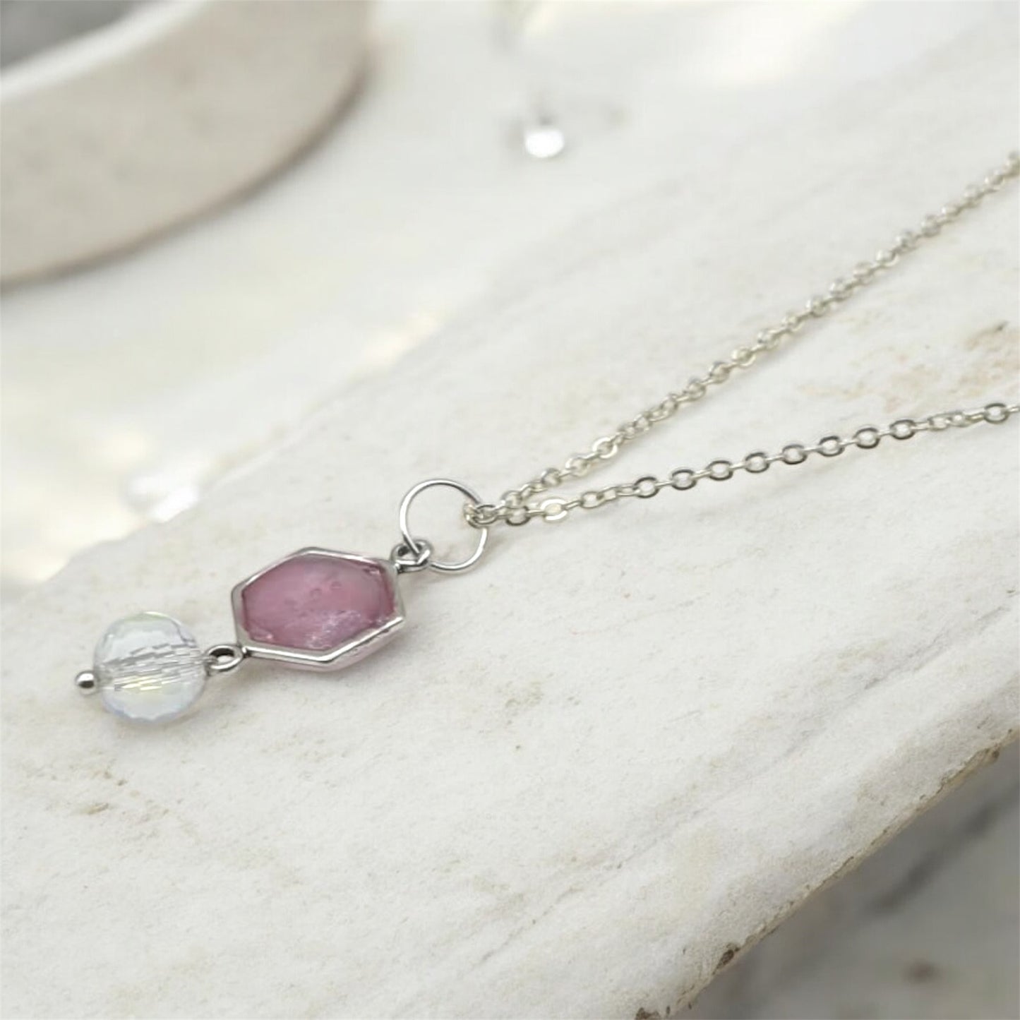 Necklace with pink and clear resin hexagon pendant on a marble surface