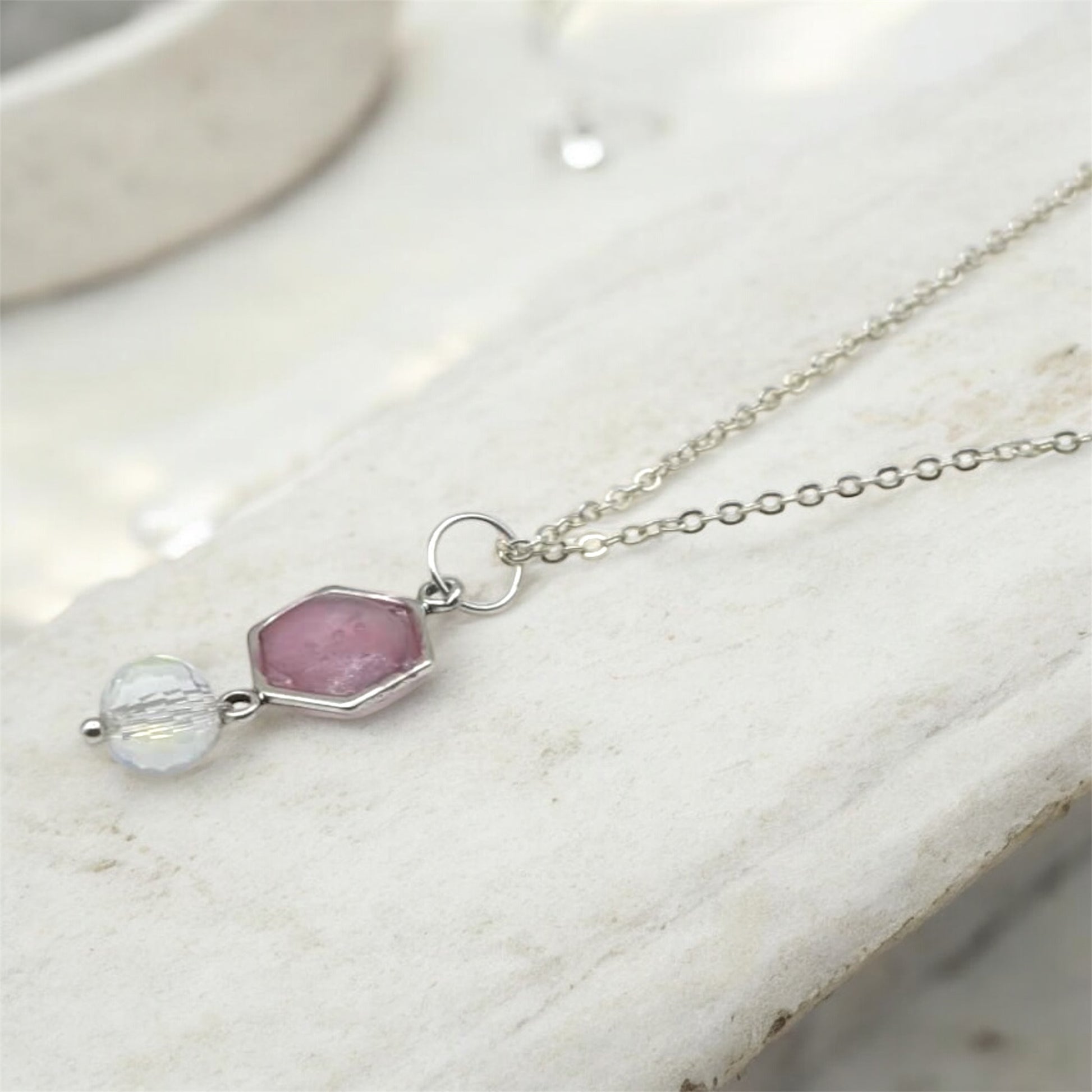 Necklace with pink and clear resin hexagon pendant on a marble surface