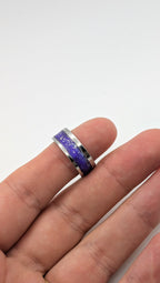 Ring with a purple and blue glittery band on a finger against a white background