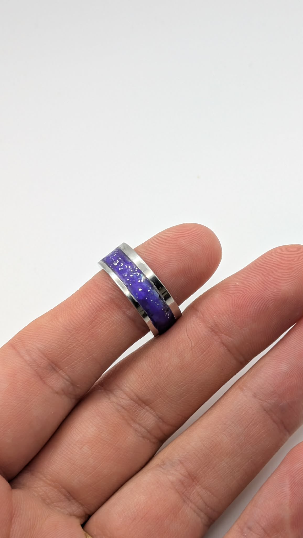 Ring with a purple and blue glittery band on a finger against a white background