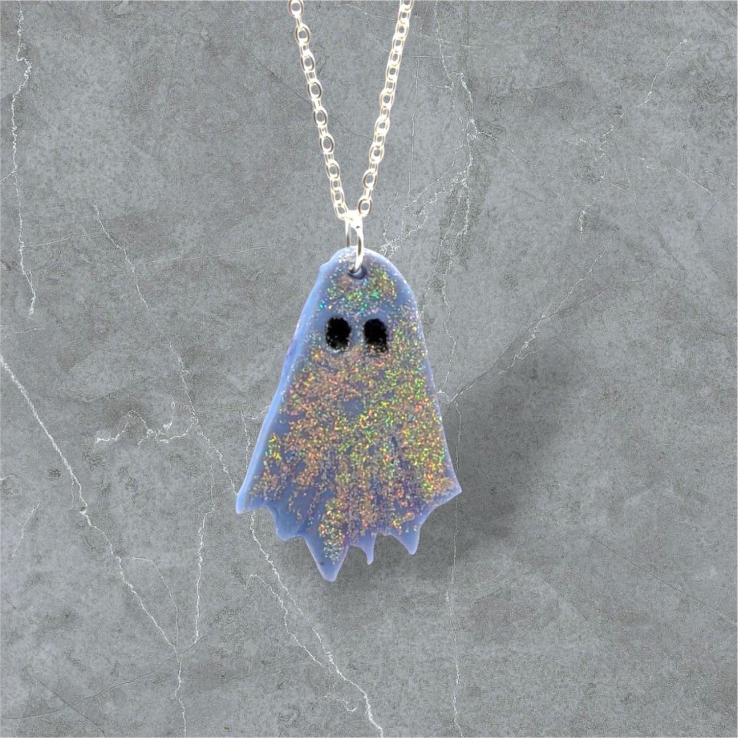 Ghost-shaped pendant on a chain against a gray marble background