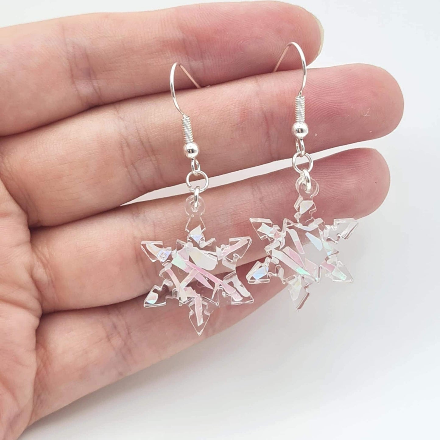 Crystal snowflake earrings held between fingers on a white background