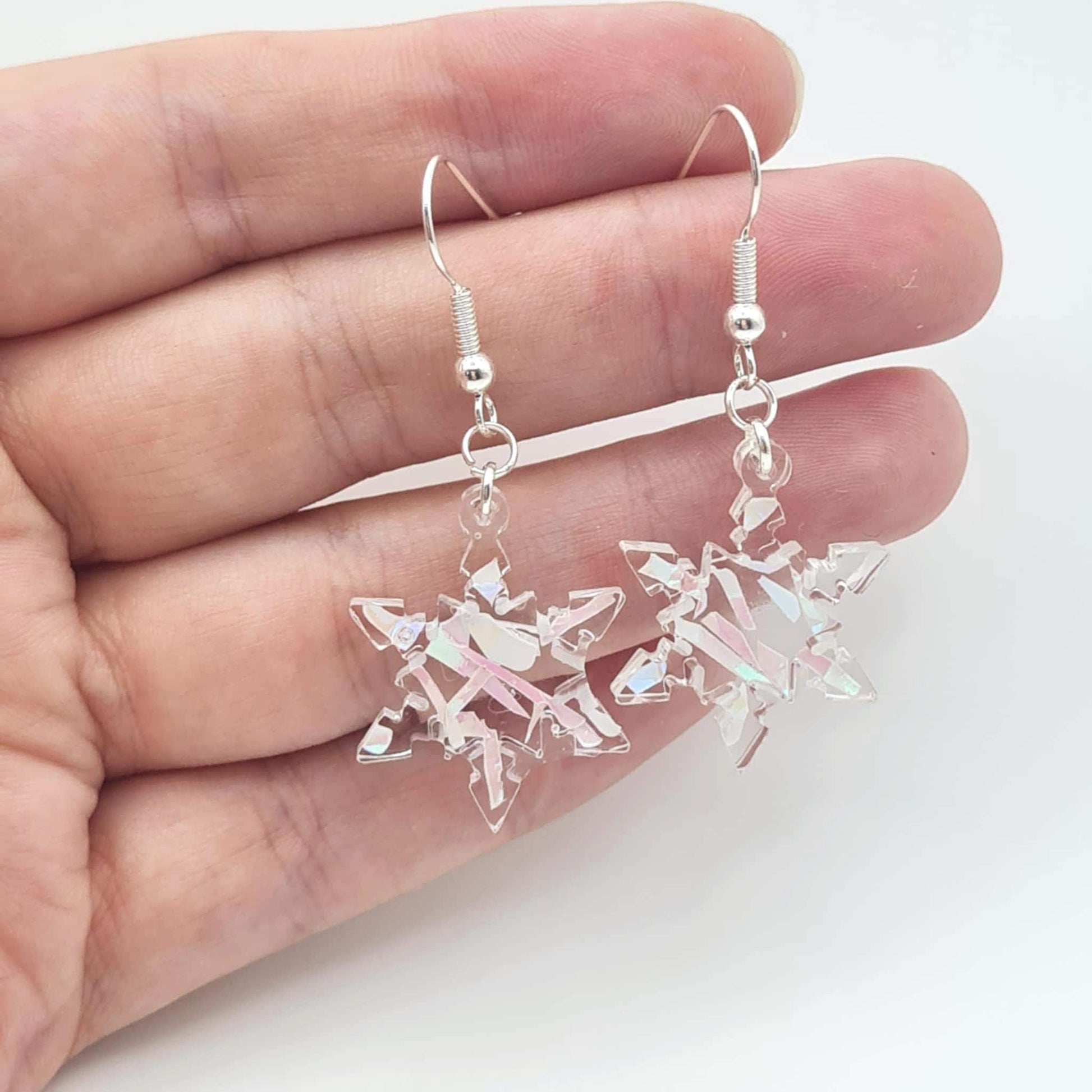 Crystal snowflake earrings held between fingers on a white background