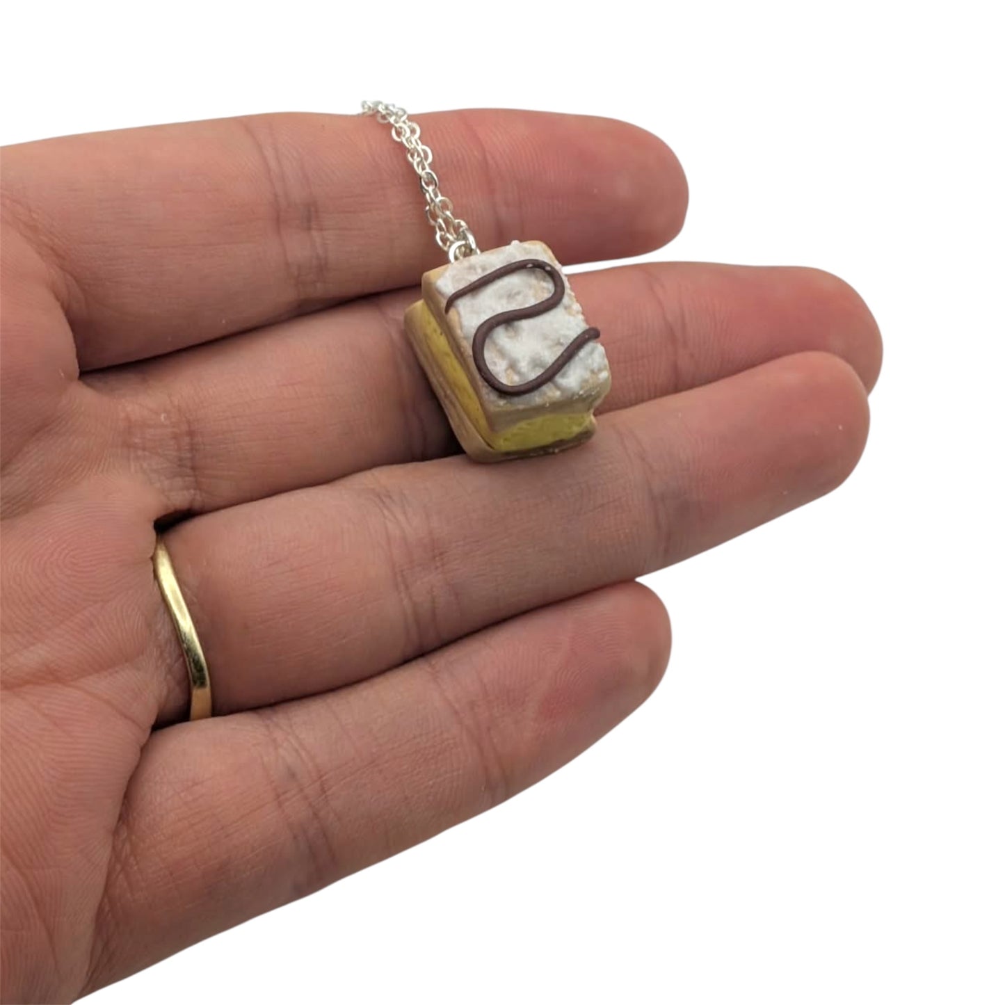 Miniature cake-shaped pendant on a chain held in a hand against a white background