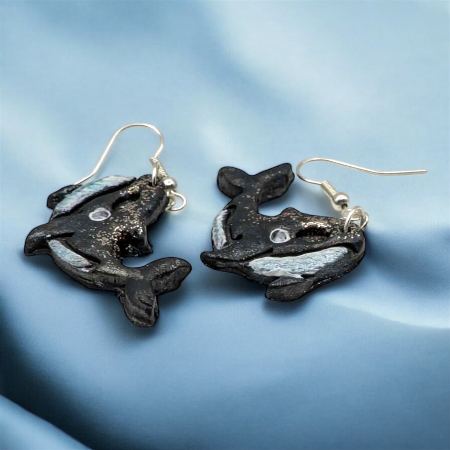 Whale-shaped earrings on a blue fabric background