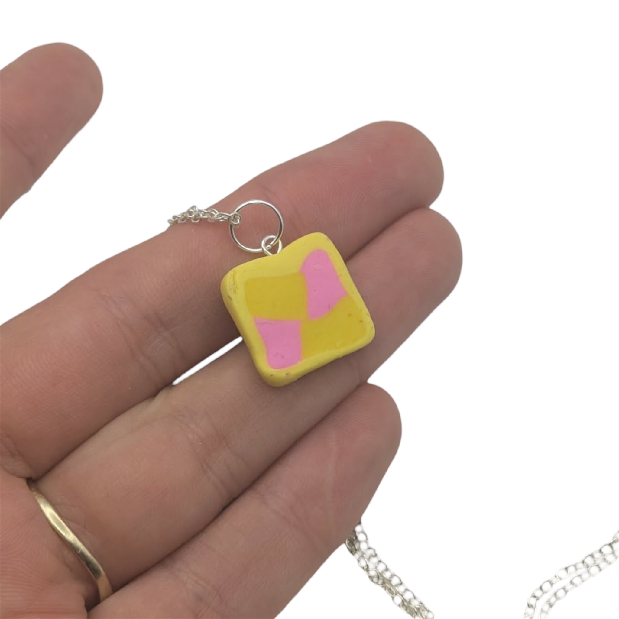 Back of cake pendant,Yellow square pendant with pink squares held in a hand on a white background