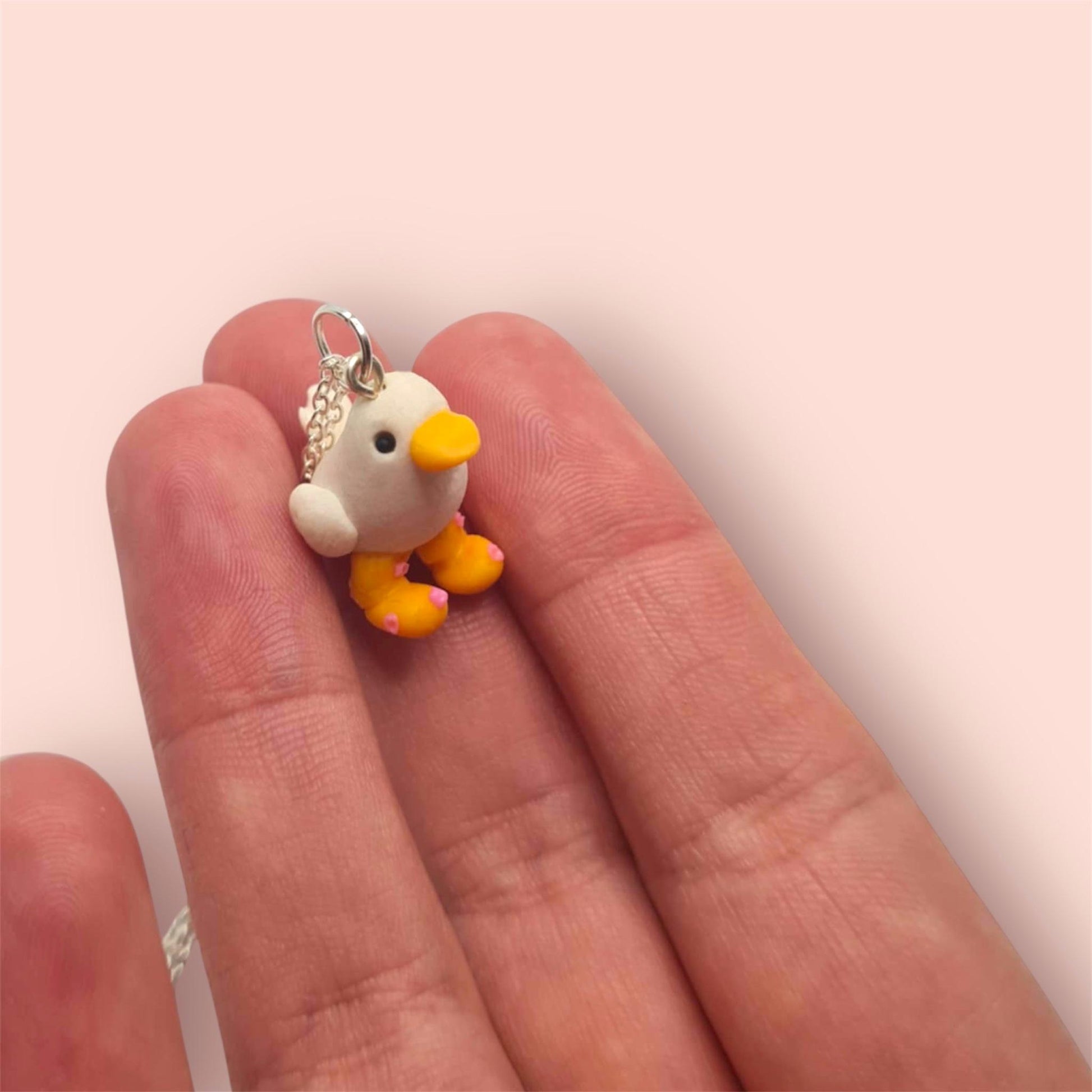 Small duck charm held between fingers on a light pink background