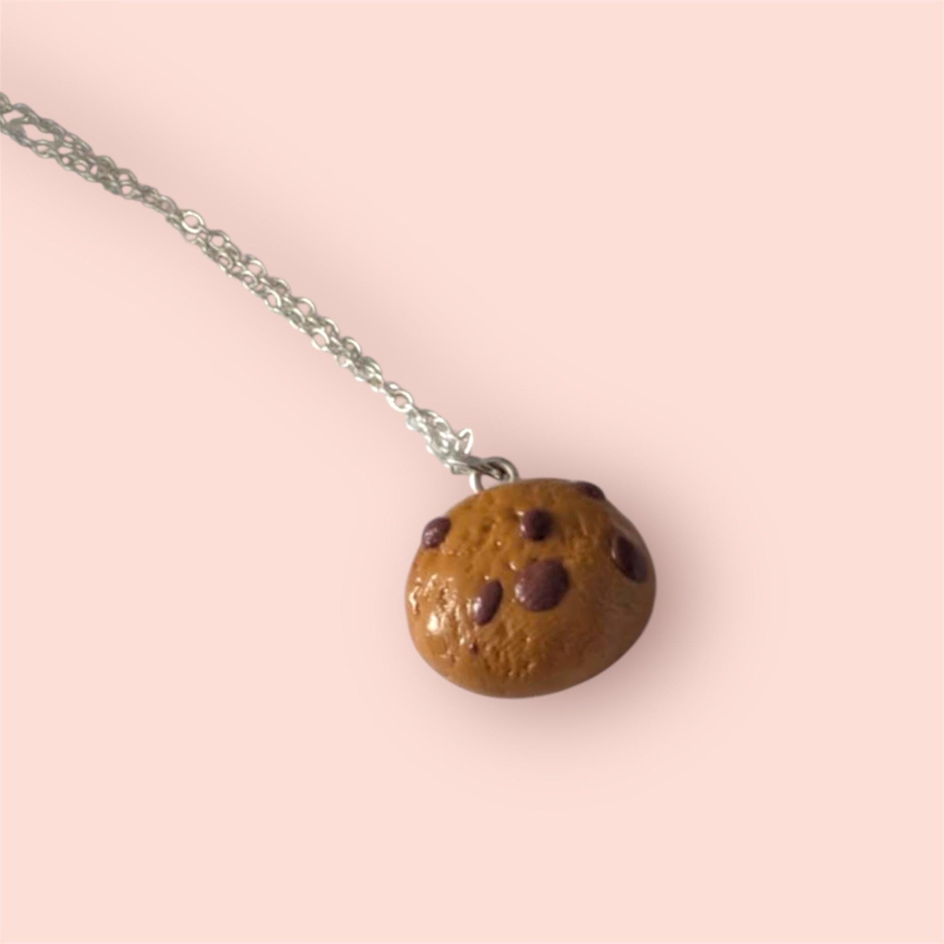 Chocolate chip cookie necklace on a pink background