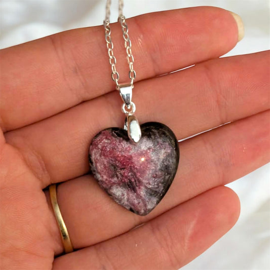Heart-shaped pink and black heart pendant on a silver chain held in a hand.