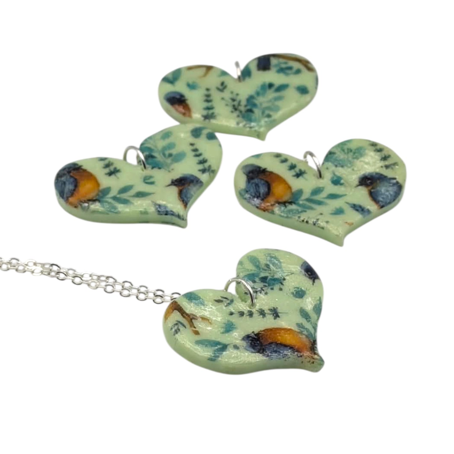 Nature pendant necklace with blue and orange birds and leaves on a green heart on a white background 