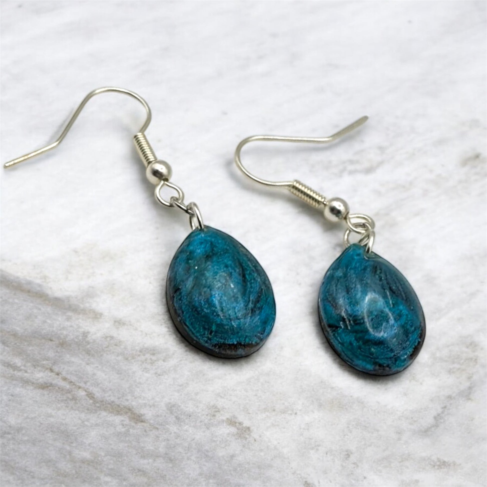 Teal resin tear drop earrings on a marble surface