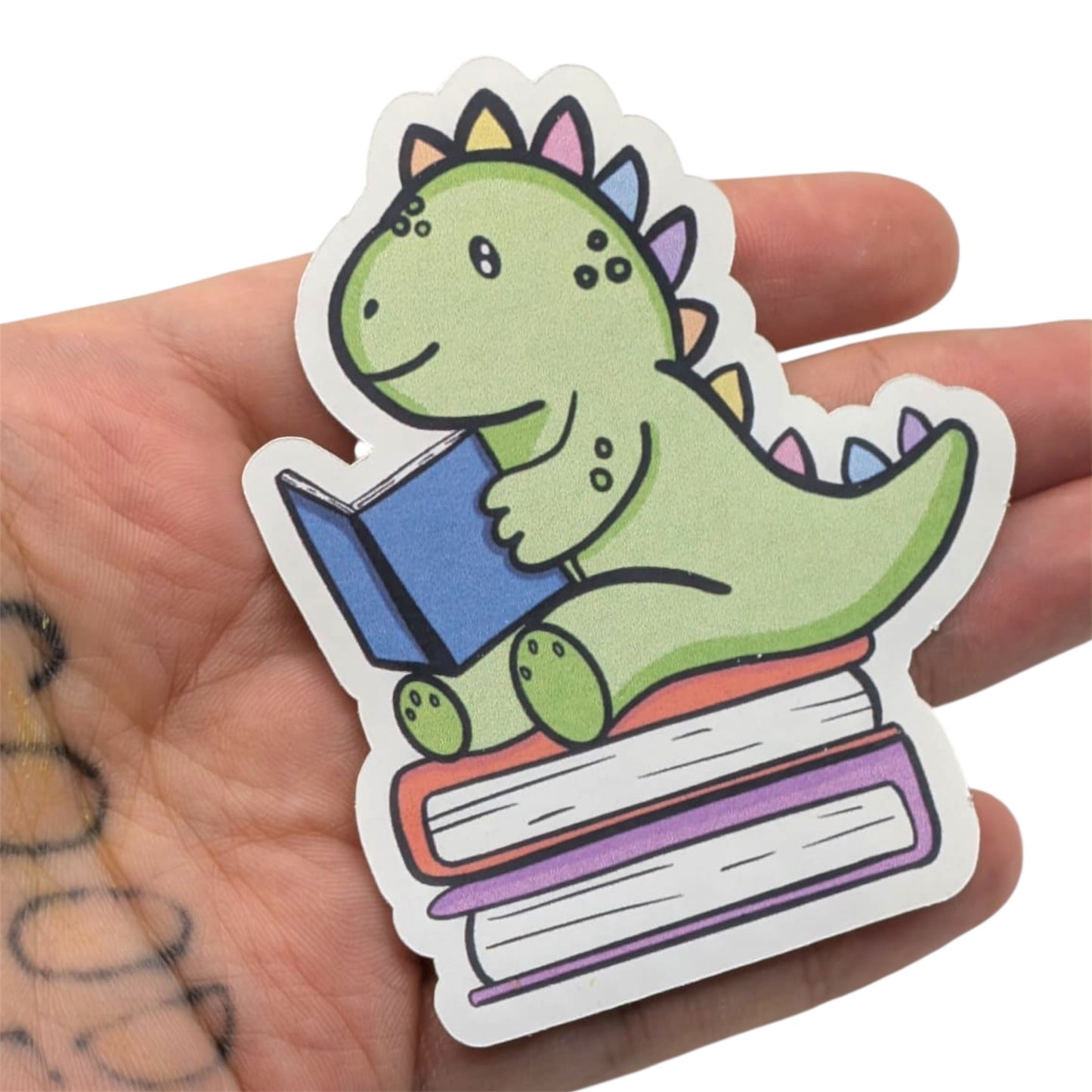 Cute green dinosaur holding books sticker held in hand on a white background 