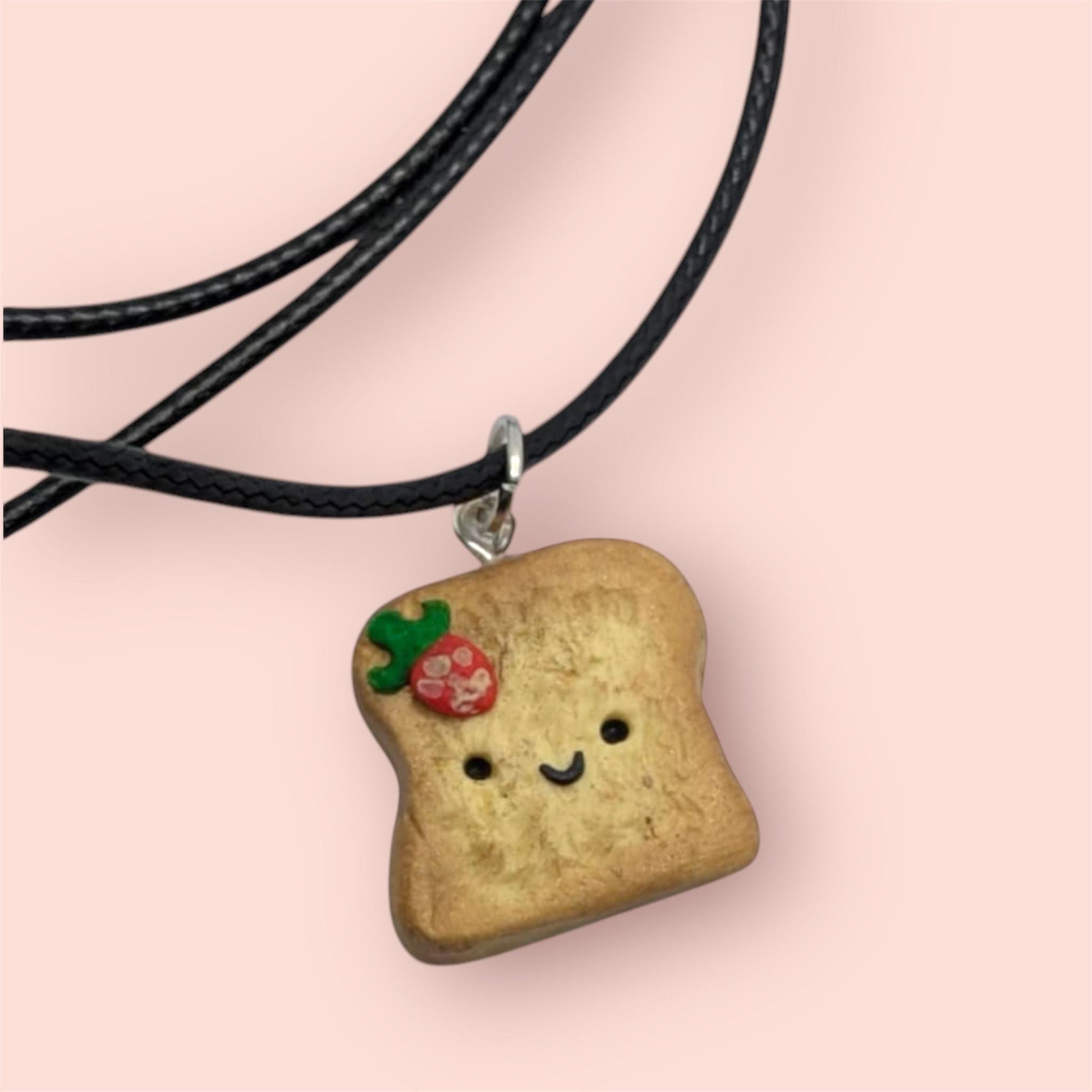 Necklace with a bread-shaped pendant featuring a smiley face on a pink background
