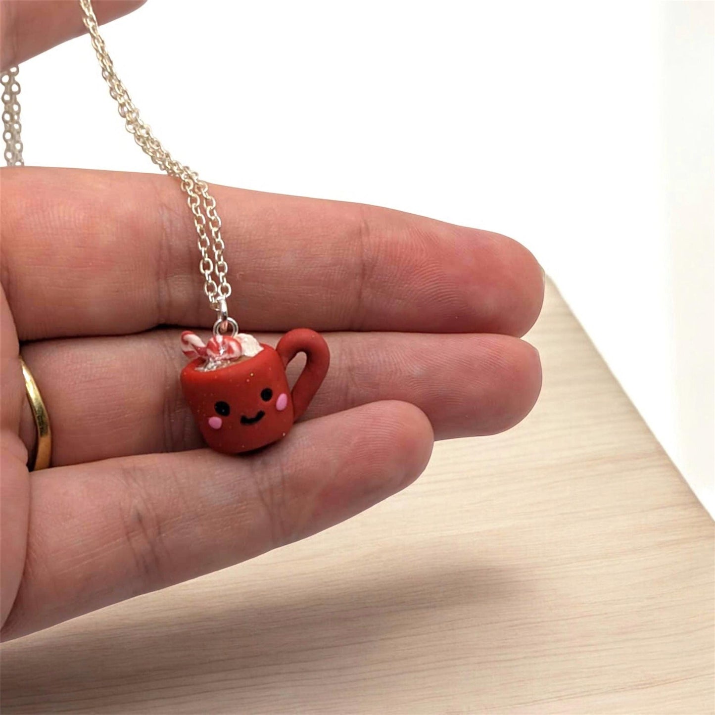 Red festive mug with candy canes and smiling ace held in hand on a wooden background 