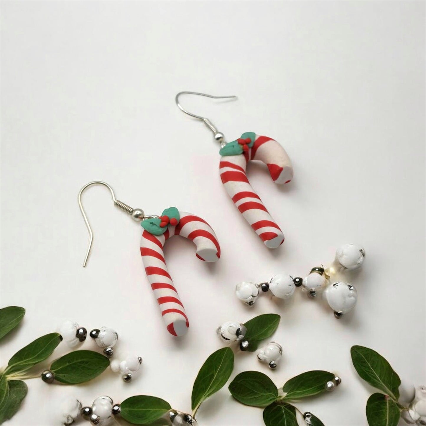 Candy cane-shaped earrings on a white background with green leaves and white berries.