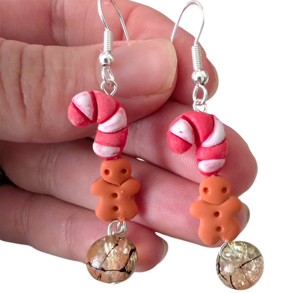 Candy cane and gingerbread man earrings held in a hand against a white background