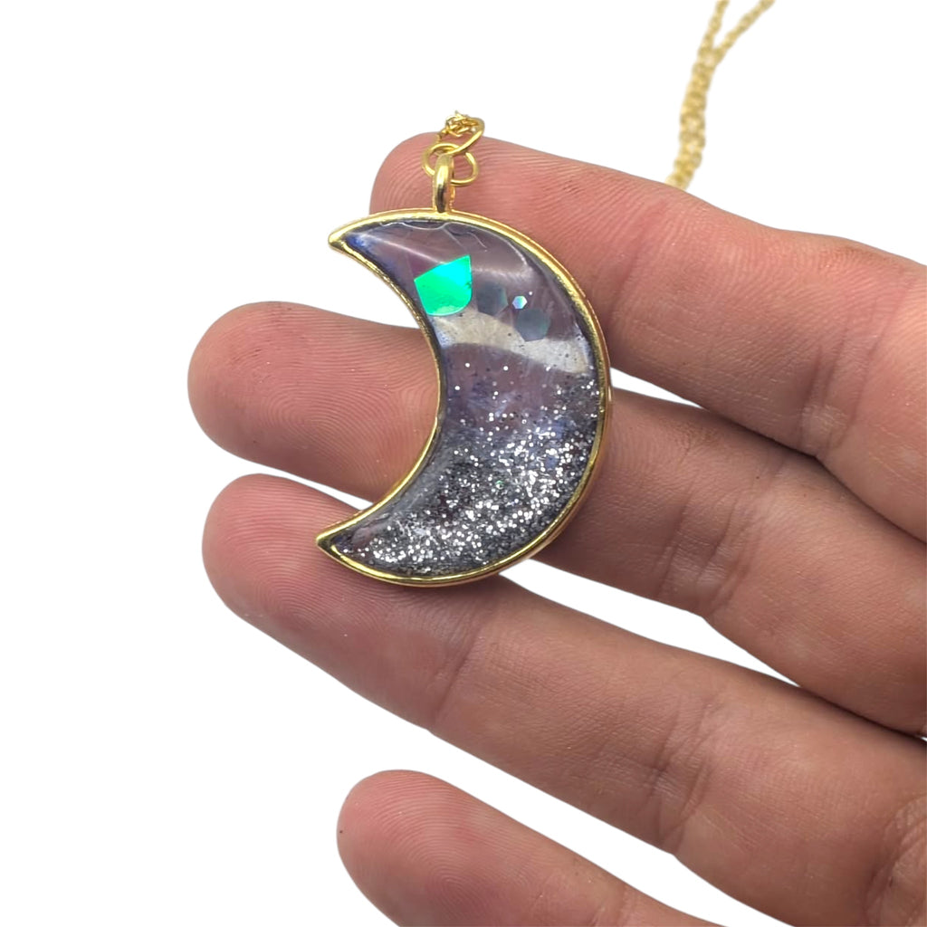 Crescent moon-shaped pendant with gold edge held between fingers on a white background