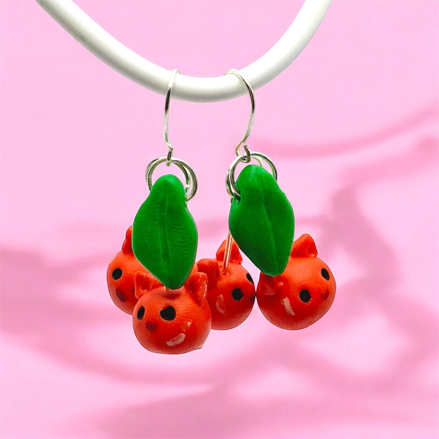 Cherry-themed earrings on a pink fabric background