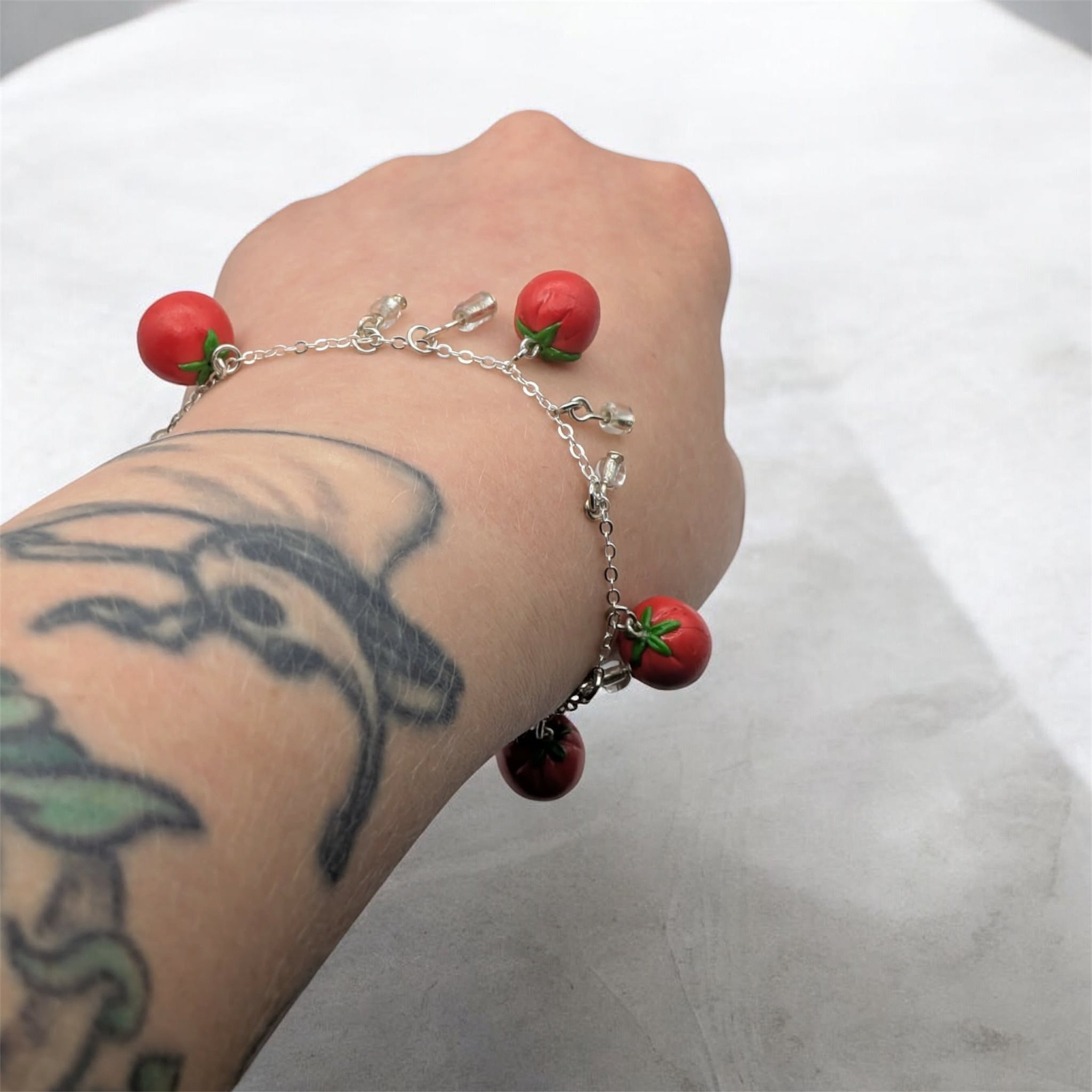 Bracelet with tomato charms on a wrist against a white background