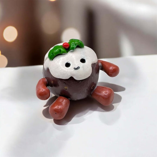 Small decorative figure of a Christmas pudding with a happy face on a white surface.