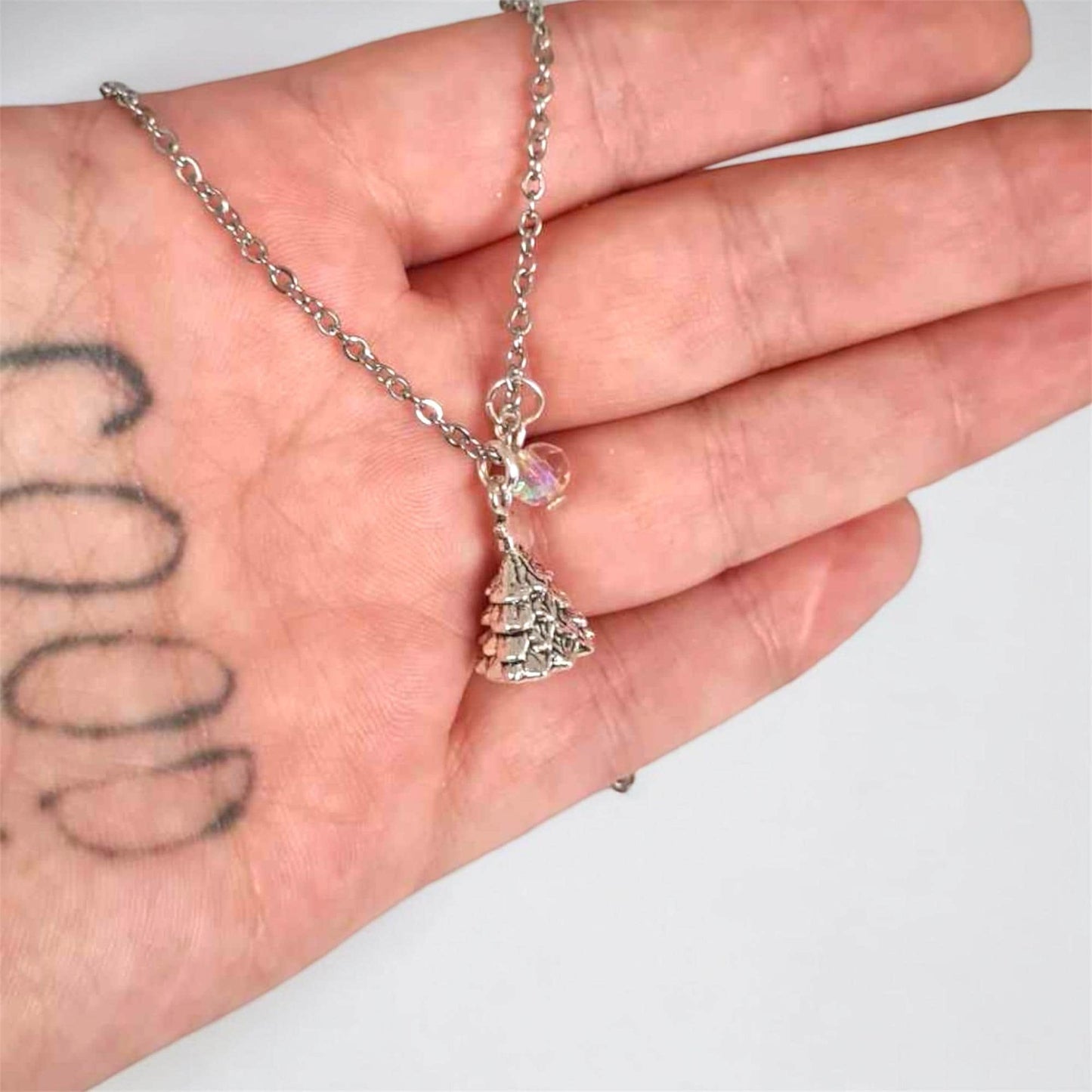 Hand holding a silver necklace with a small pendant against a plain background