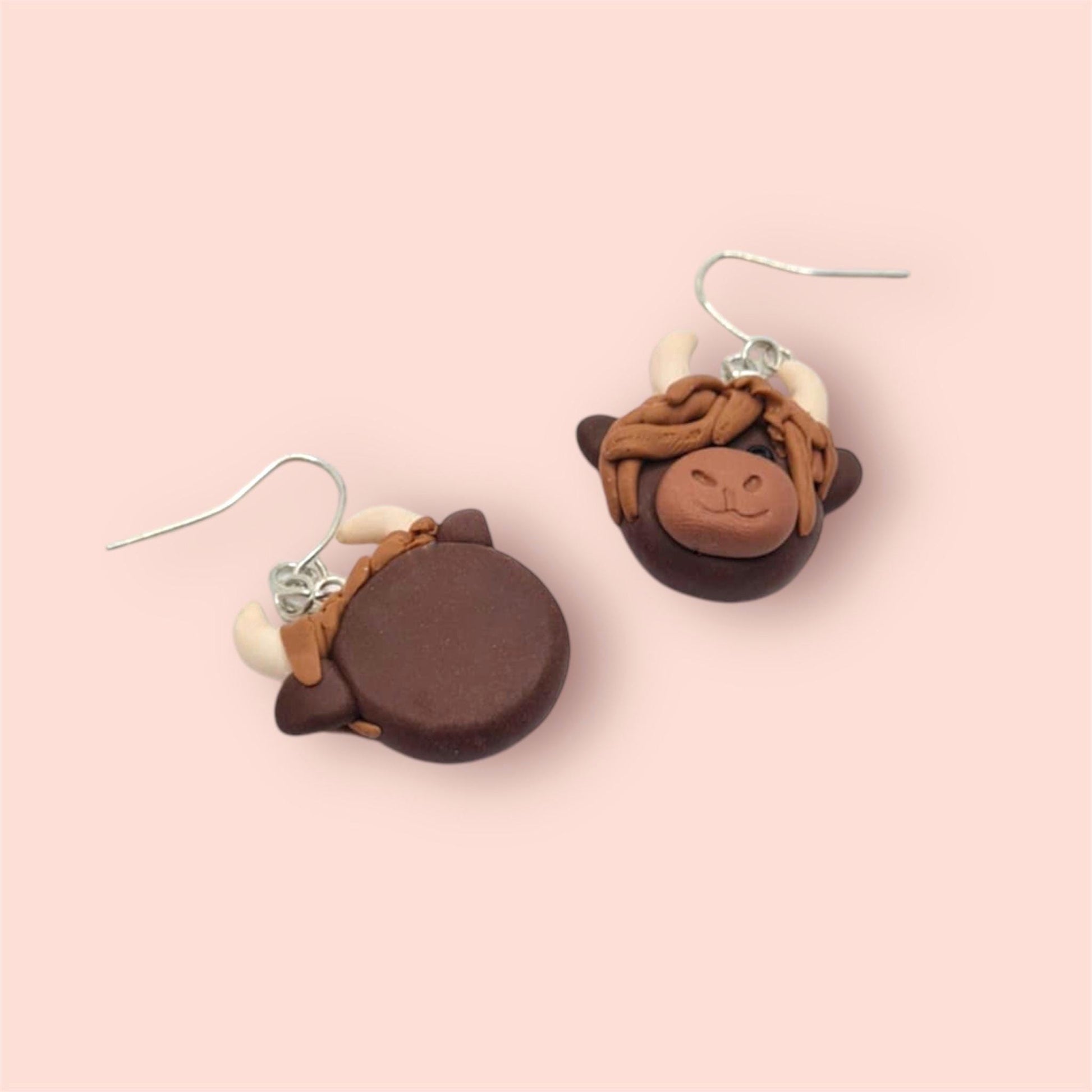 Pair of brown cow-shaped earrings on a pink background